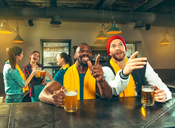 Sport, people, leisure, friendship and entertainment concept - happy football fans or male friends drinking beer and celebrating victory at bar or pub