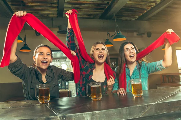 Sport, people, leisure, friendship and entertainment concept - happy football fans or female friends drinking beer and celebrating victory at bar or pub