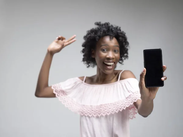 Retrato de una chica afro casual confiada que muestra el teléfono móvil de pantalla en blanco —  Fotos de Stock