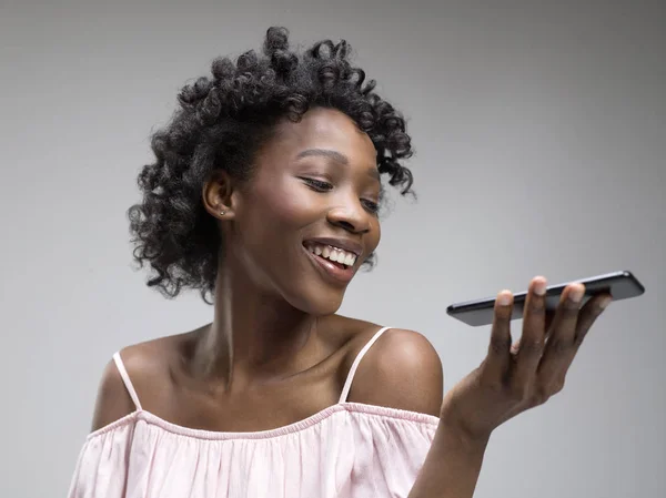Retrato interior de una atractiva joven negra sosteniendo un smartphone en blanco —  Fotos de Stock