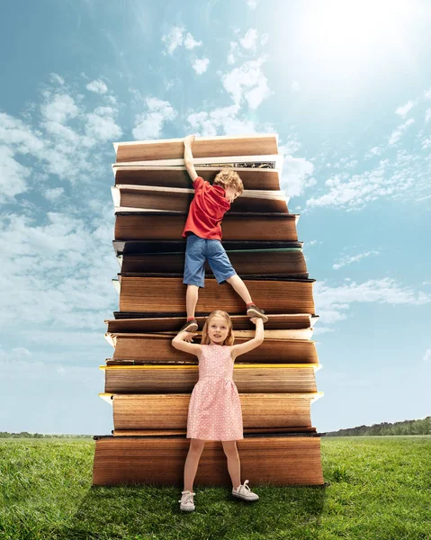 Menina e menino subindo na torre feita de grandes livros — Fotografia de Stock