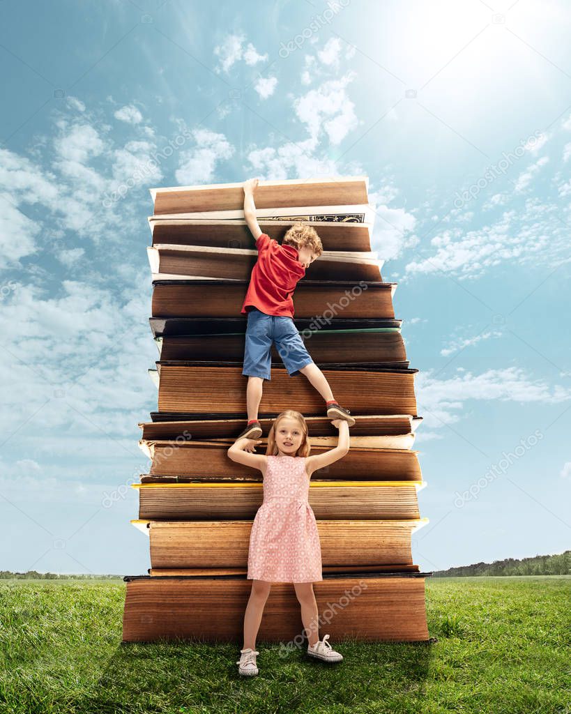 Little girl and boy climbing on the tower made of big books