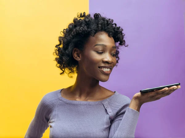 Retrato interno de atraente jovem mulher negra segurando smartphone em branco — Fotografia de Stock