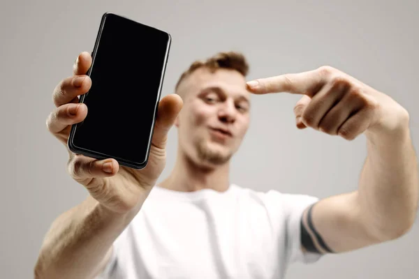Stilig ung visar smartphone skärmen isolerade på grå bakgrund i chock med en överraskning ansikte — Stockfoto