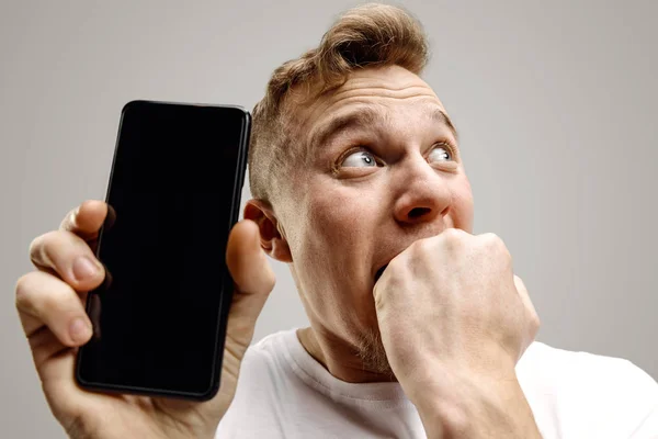 年轻英俊的男子显示智能手机屏幕孤立在灰色背景与一个惊喜的脸 — 图库照片