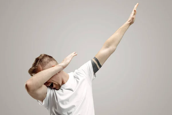 Jovem faz o movimento dab com os braços em um fundo cinza . — Fotografia de Stock