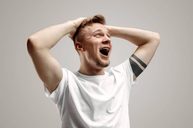 The young emotional angry man screaming on garay studio background clipart