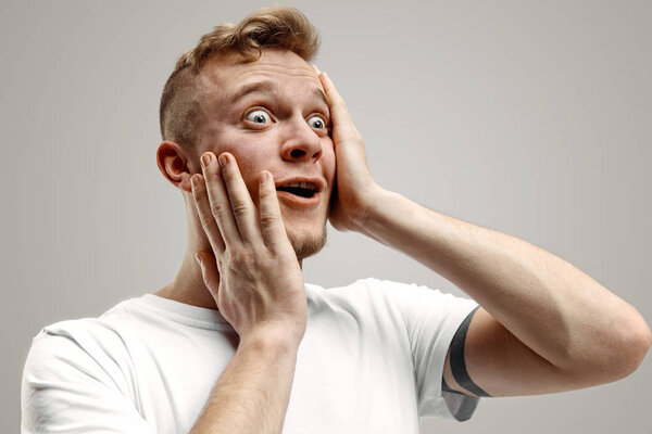 Молодой привлекательный мужчина, выглядящий удивленным, изолированным на сером
