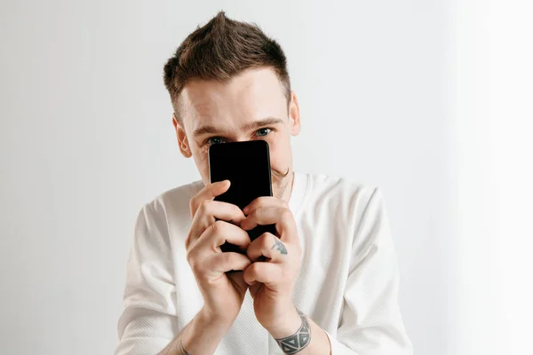 Joven hombre guapo mostrando la pantalla del teléfono inteligente aislado sobre fondo gris en shock con una cara sorpresa — Foto de Stock