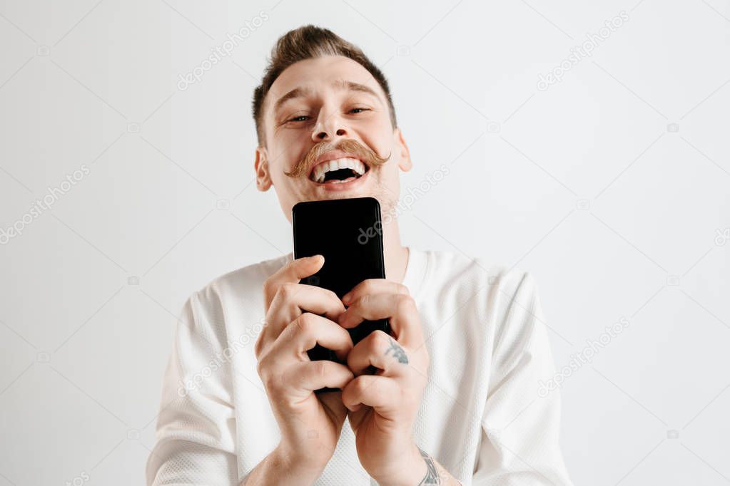 Young handsome man showing smartphone screen isolated on gray background in shock with a surprise face