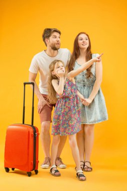 Mutlu anne-baba ile kızı ve bavul üzerinde sarı arka plan izole stüdyosu