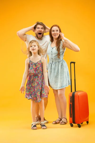 Счастливый родитель с дочерью и чемоданом в студии изолированы на желтом фоне — стоковое фото