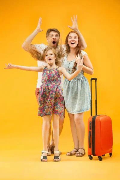 Счастливый родитель с дочерью и чемоданом в студии изолированы на желтом фоне — стоковое фото