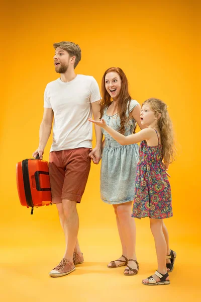 Padres felices con hija y maleta en el estudio aislados sobre fondo amarillo — Foto de Stock