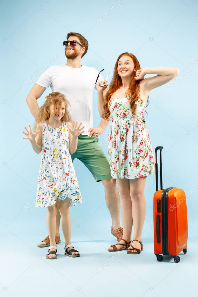 Happy parent with daughter and suitcase at studio isolated on blue background