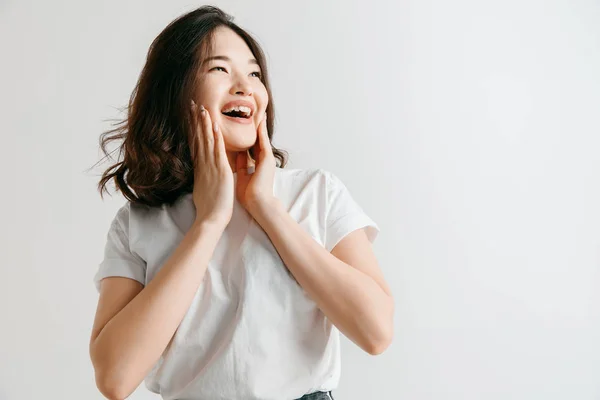 A mulher asiática feliz de pé e sorrindo contra fundo cinza . — Fotografia de Stock