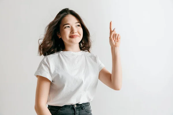 De gelukkige Aziatische vrouw permanent en glimlachend tegen de grijze achtergrond. — Stockfoto