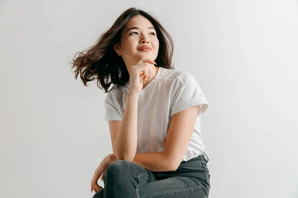 A mulher asiática feliz de pé e sorrindo contra fundo cinza . — Fotografia de Stock