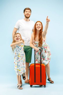 Mutlu anne-baba ile kızı ve bavul üzerinde mavi arka plan izole stüdyosu