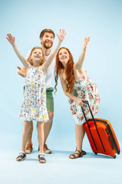 Mutlu anne-baba ile kızı ve bavul üzerinde mavi arka plan izole stüdyosu