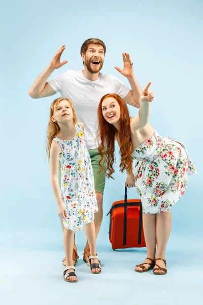 Padres felices con hija y maleta en el estudio aislados sobre fondo azul — Foto de Stock