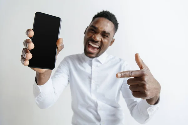 Vonzó fekete-afrikai fiatalember rózsaszín háttér, elszigetelt gazdaság üres smartphone, mosolyogva kamera, bemutatás képernyő, érzés, boldog és meglepett beltéri portré. Emberi érzések, arc — Stock Fotó