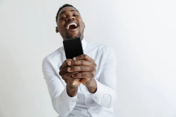 Retrato interior de un atractivo joven africano negro aislado sobre fondo rosa, sosteniendo un smartphone en blanco, sonriendo a la cámara, mostrando la pantalla, sintiéndose feliz y sorprendido. Emociones humanas, faciales — Foto de Stock