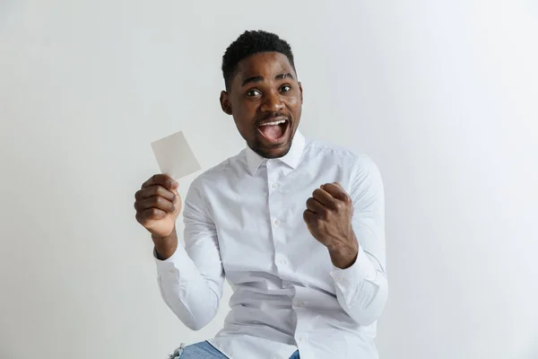 Ein junger Afro-Mann mit einem überraschend fröhlichen Gesichtsausdruck gewann eine Wette auf grauen Studiohintergrund. menschliche Gesichtsbewegungen und Wettkonzept. — Stockfoto