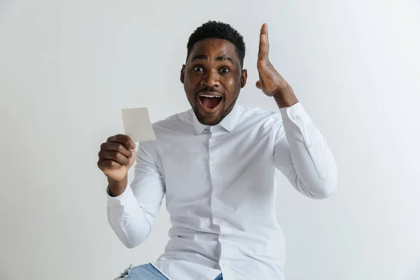 Joven hombre afro con una expresión feliz sorprendido ganó una apuesta en fondo gris estudio. Emociones faciales humanas y concepto de apuestas . — Foto de Stock