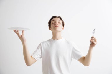 Boş tabak ve gri arka plan üzerinde izole çatal tutan genç gülümseyen çekici adam.