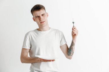 Boş tabak ve gri arka plan üzerinde izole çatal tutan genç üzgün çekici adam.