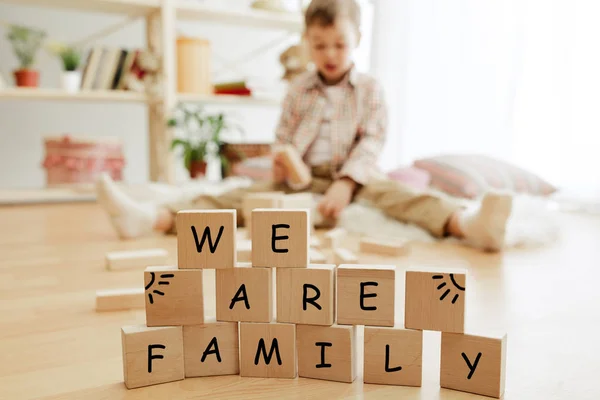 Wooden cubes with words WE ARE FAMILY in hands of little boy — Stock Photo, Image