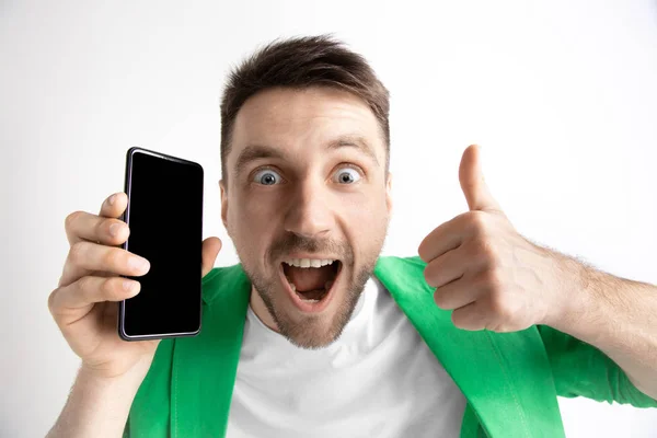 Junger gutaussehender Mann zeigt Smartphone-Bildschirm und signiert ok isoliert auf grauem Hintergrund — Stockfoto