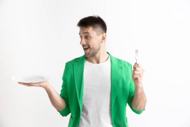Boş tabak ve gri arka plan üzerinde izole çatal tutan genç gülümseyen çekici adam.