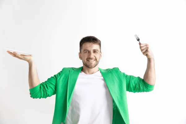 Jovem sorrindo cara atraente segurando prato vazio e garfo isolado no fundo cinza . — Fotografia de Stock