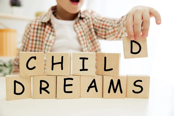 Trä kuber med ord barn drömmar i händerna på liten pojke — Stockfoto