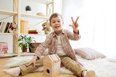 Katta oturan küçük bir çocuk. Evde ahşap küpleriyle yakışıklı palying