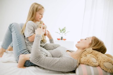 Genç anne ve küçük kızı sarılma ve yatakta öpüşme