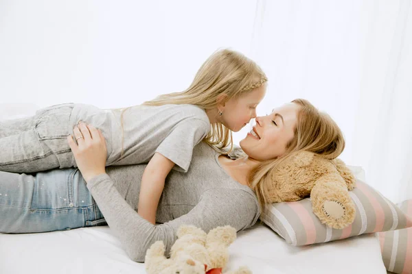 Jovem mãe e sua filhinha abraçando e beijando na cama — Fotografia de Stock