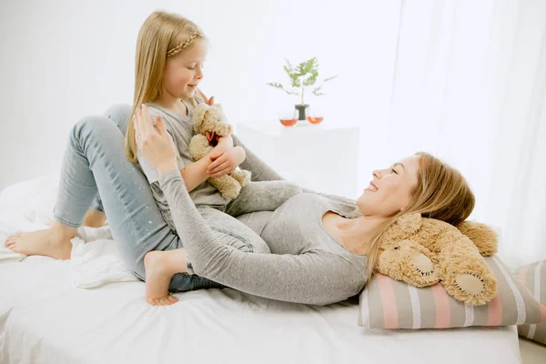 Giovane madre e la sua piccola figlia abbracciare e baciare sul letto — Foto Stock