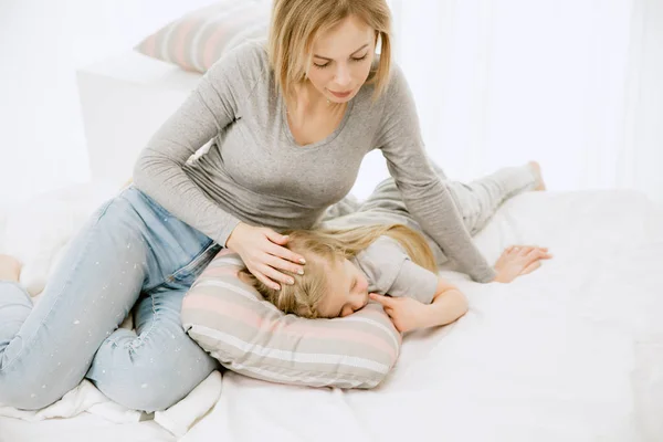 Mladá matka a její malá dcera objímat a líbat na posteli — Stock fotografie