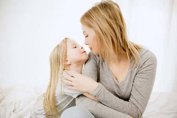 Junge Mutter und ihre kleine Tochter umarmen und küssen sich auf dem Bett — Stockfoto