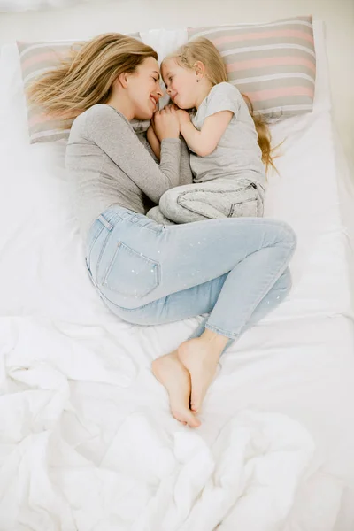 Ung mamma och hennes lilla dotter kramas och kyssas på säng — Stockfoto
