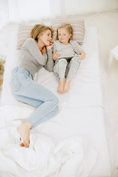 Молода мама і її маленька дочка обіймають і цілують на ліжку — стокове фото