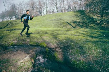 Bir park veya ormandaki ağaçlar arka plan karşı koşan adam.