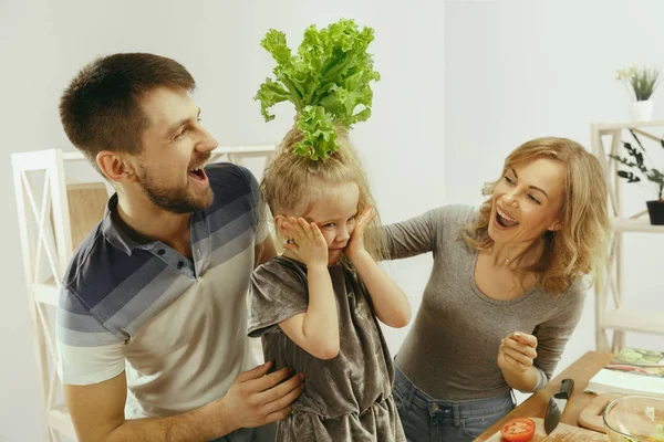 Ładna dziewczynka i jej piękne rodzice są cięcia warzyw w kuchni w domu — Zdjęcie stockowe