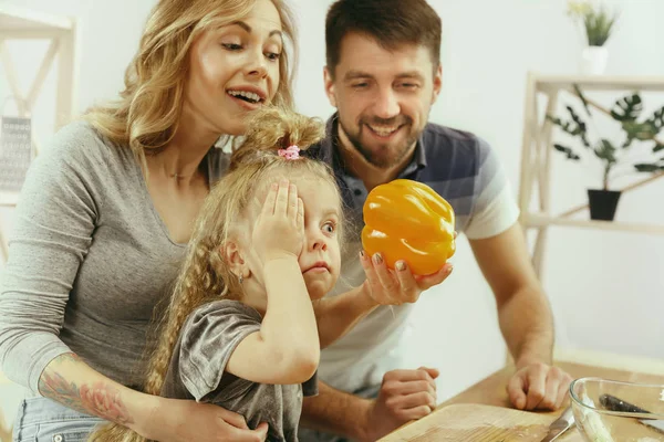 Linda niña y sus hermosos padres están cortando verduras en la cocina en casa —  Fotos de Stock