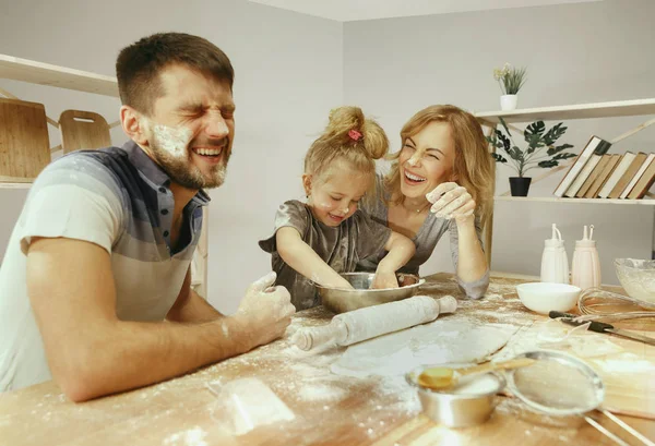 Cute little girl and her beautiful parents preparing the dough for the cake in kitchen at home