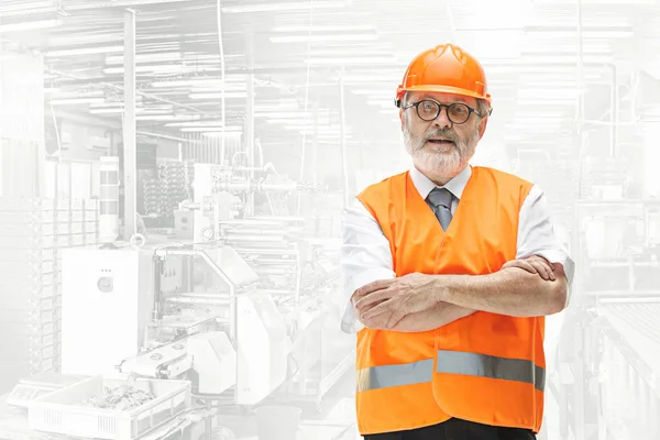 Construtor sênior profissional em capacete laranja contra fundo industrial — Fotografia de Stock