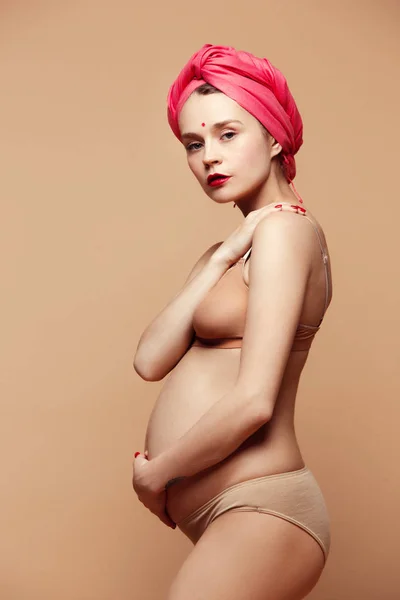 Mladá krásná těhotná žena, která pózala na hnědém pozadí — Stock fotografie